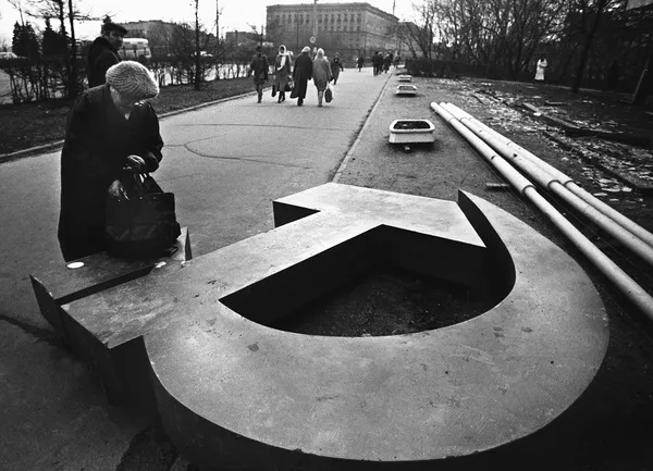 Black and white photo of a Soviet woman looking at fallen hammer and sickle emblem.
